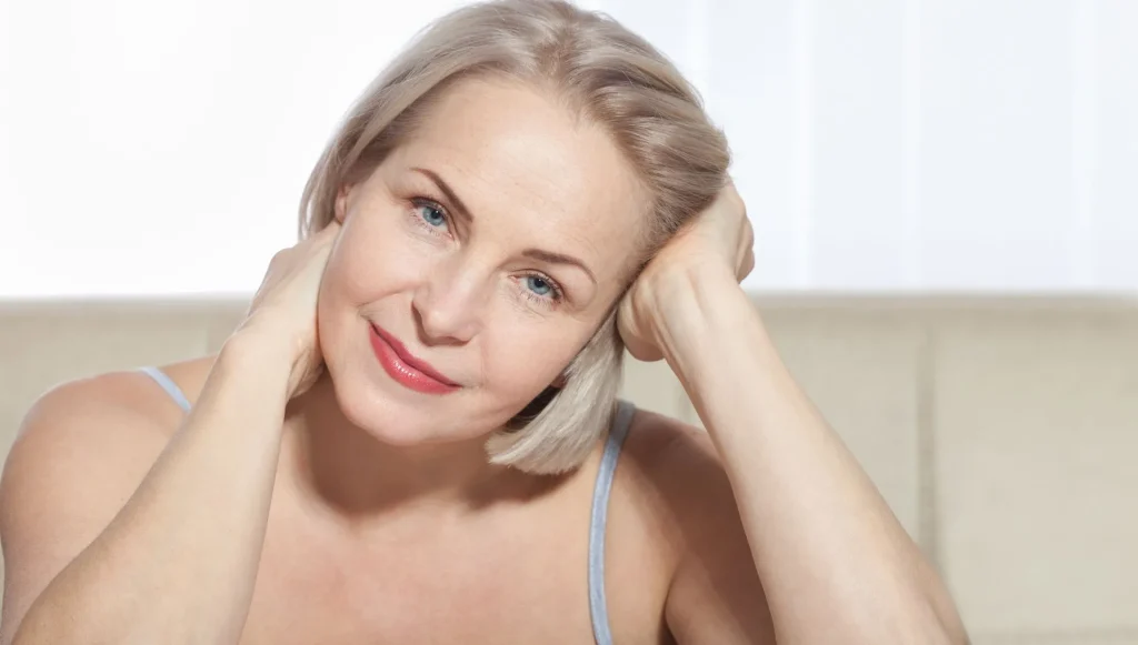 A woman is touching her face with her hands and smiling.